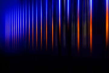 Abstract blurred background - vertical parallel color stripes orange, light, blue on black.
