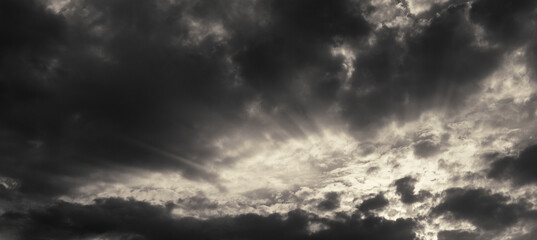 Dark rain clouds and sun rays at sunset. Web banner.