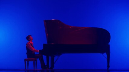 Pianist in red neon light sitting and playing on the black grand piano on dark concert stage under bright spotlight, isolated on blue studio background.