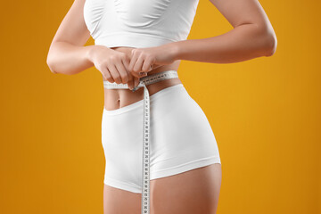 Weight loss. Woman measuring her slim waist with tape on yellow background, closeup