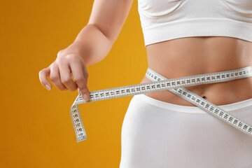 Weight loss. Woman measuring her slim waist with tape on yellow background, closeup