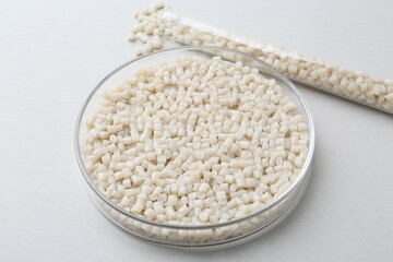 Plastic granules in petri dish and test tube on gray background, closeup