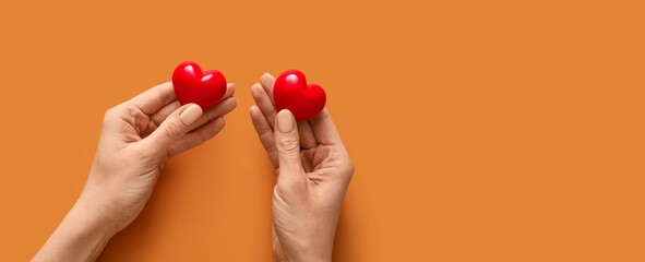 Hands holding red hearts on orange background with space for text