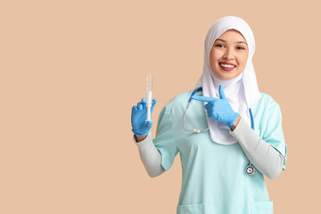 Female Muslim doctor in hijab pointing at syringe on beige background. World Hijab Day concept