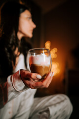 Relaxing Woman Enjoys Cappuccino With Marshmallows While Lounging in Bed Surrounded by a Festive Christmas Tree and Warm Lights