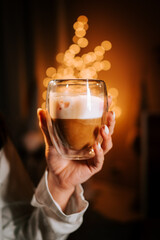 Woman Enjoying a Warm Cappuccino With Marshmallows While Cozy in Bed Near a Beautifully Decorated Christmas Tree at Night