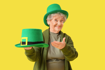 Happy senior woman with leprechaun hats on yellow background. St. Patrick's Day celebration