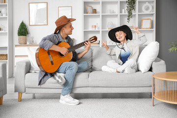 Cute little boy with his father in cowboy hats playing guitar at home