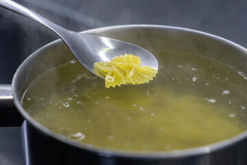 boiled farfalle pasta lifted from steaming pot with silver spoon over hot water
