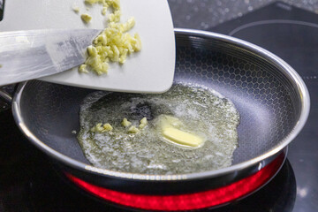 adding minced garlic to melted butter in a frying pan on a hot stovetop