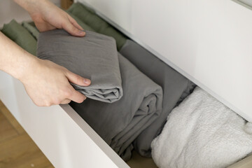 folding gray bedsheets into drawer with hands carefully organizing fabric for tidy and clean storage arrangement at home