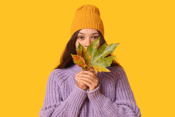 Beautiful young Asian woman with autumn leaves on yellow background