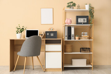 Interior of room with workplace, shelving unit, laptop and safe boxes on table near beige wall