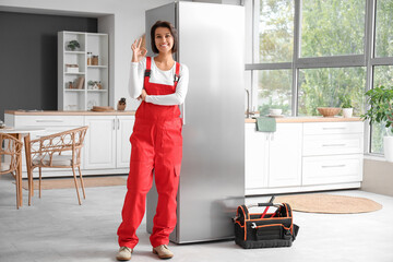 Female worker showing OK near fridge in kitchen
