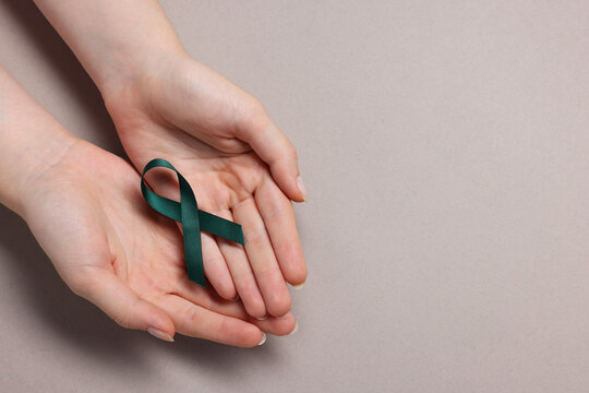 Woman with teal ribbon on grey background, top view with space for text. Ovarian cancer and gynecological disorders awareness
