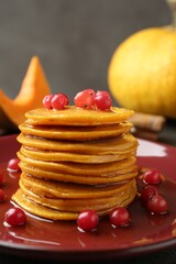 Tasty pumpkin pancakes with cranberries and honey on table, closeup