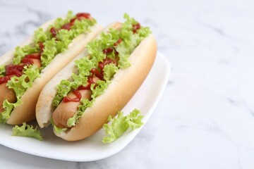 Tasty hot dogs with lettuce and ketchup on white marble table, closeup. Space for text