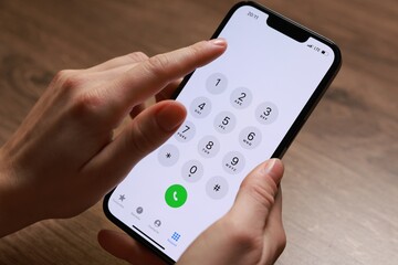 Woman dialing number on smartphone at wooden table, closeup