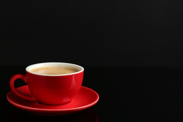 Red cup with coffee on black background, space for text