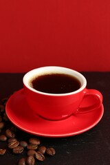Red cup with coffee and roasted beans on black table