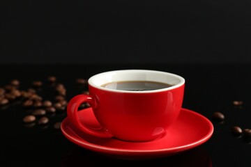 Red cup with coffee and roasted beans on black background, closeup