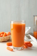 Fresh carrot juice in glass and vegetables on white table against gray background