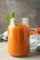 Fresh carrot juice and mint in mason jar on gray textured table