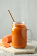 Fresh carrot juice in mason jar and vegetable on gray textured table