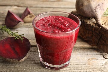 Fresh beetroot smoothie in glass, rosemary and cut vegetables on wooden table, closeup
