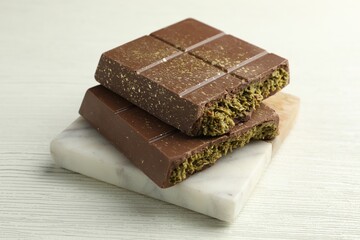 Pieces of tasty Dubai chocolate with pistachios and knafeh on white wooden table, closeup