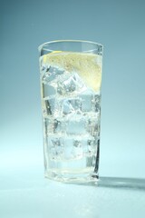 Soda water with lemon and ice cubes in glass on light blue background