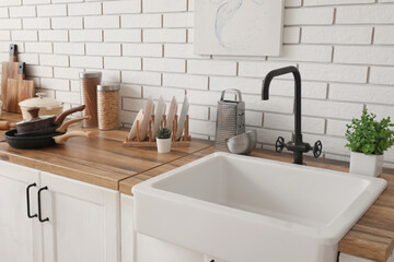 Sink, houseplants and utensils on counter near white brick wall in kitchen