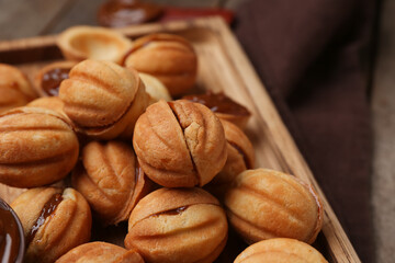 Cutting board of sweet walnut shaped cookies with boiled condensed milk on wooden background, closeup