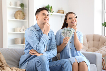 Dreaming young couple with money sitting on sofa at home