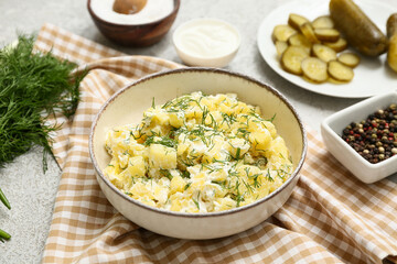 Bowl of tasty potato salad with dill, peppercorns, sour cream and pickled cucumbers on grey grunge background