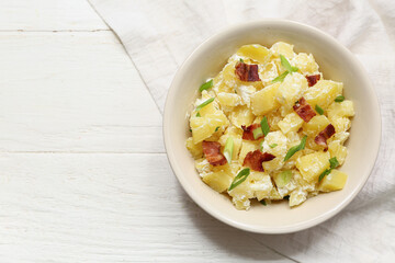 Bowl of tasty potato salad with bacon and green onion on white wooden background