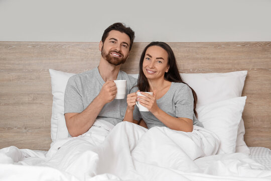 Morning of loving couple with cups of coffee lying in bedroom - Powered by Adobe