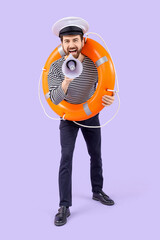 Male sailor with rescue ring and megaphone on lilac background