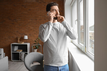 Portrait of worried man talking by phone near window