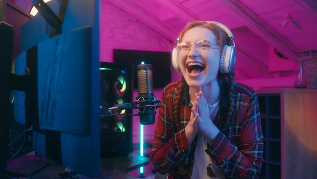 Happy girl teen Caucasian woman female blogger vlogger influencer radio streamer in headphones neon studio online stream computer video game gaming addict cyber sport win celebrate victory scream goal