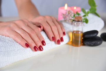 Female hands with red nail polish on a towel in a beauty studio, surrounded by decorations. Manicure and beauty concept