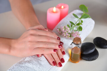 Female hands with red nail polish on a towel in a beauty studio on a white desk with decorations. Manicure and beauty concept