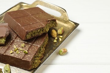 Pieces of Dubai chocolate bar with pistachios and knafeh on white wooden table, closeup. Space for text