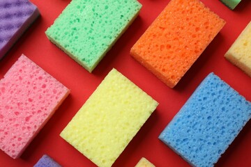 Colorful sponges on red background, flat lay. Cleaning tool