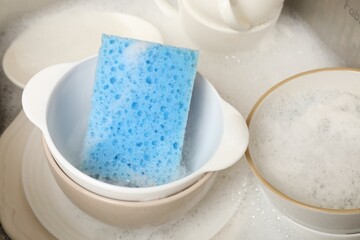 Blue sponge, dishes and foam in sink, closeup