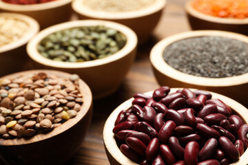 Different superfood products in bowls on wooden table, closeup