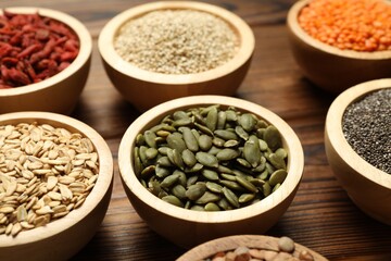 Different superfood products in bowls on wooden table, closeup
