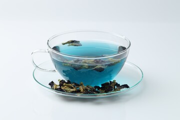Fresh butterfly pea flower tea in cup and dry petals on white table, closeup