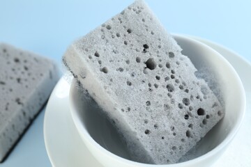 Sponge with foam and dishware on light blue background, closeup