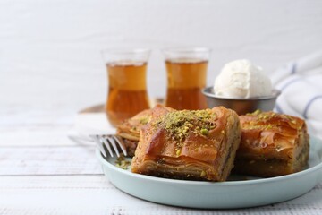 Delicious baklava with crushed nuts and ice cream on white wooden table, closeup. Space for text